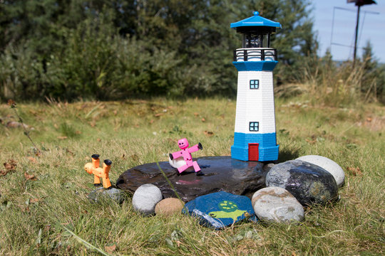 Stickbot toys posed on rocks near lighthouse in summer sunshine, whimsy, cute, macro.