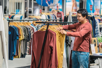 Smart asian man with beard choosing clothes in clothing store at shopping center, looking colorful t-sshirts , Fashion and Consumerism Concept.