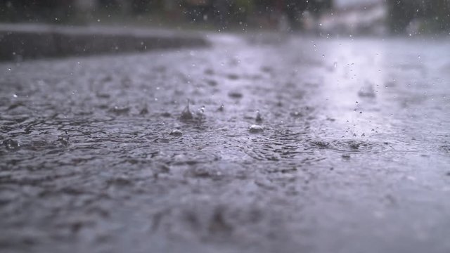 SLOW MOTION CLOSE UP: Autumn rain water drops falling into big puddle on asphalt, flooding the street. Road floods due to the heavy rain in wet season. Raindrops falling down onto submerged road