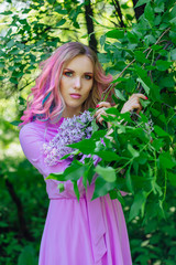 Beautiful girl with colorful dyed hair and perfect makeup standig next to lilac bush