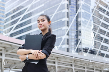 Fototapeta premium Confident young Asian business woman with document folder standing at outside office.