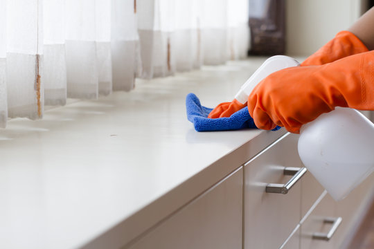 Hand in gloves spraying a cleanser to a wooden furniture for cleaning a dust in bedroom. house cleaning and housekeeping concept.