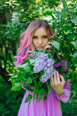 Beautiful girl with colorful dyed hair and perfect makeup standig next to lilac bush