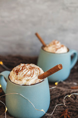 Mug of coffee, cocoa or hot chocolate with whipped cream and cinnamon on scarf with leaves, garland, anise star. Pumpkin latte - cozy drink for cold autumn or winter.