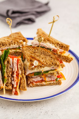 Ham, vegetables and cheese club sandwiches on a white plate, white background.