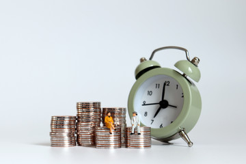 A preparatory concept for post-retirement cost of living. Miniature men and women sitting on a pile of coins with alarm clocks.