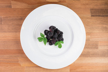 Large blackberries. Blackberries in a white plate on a wooden table.