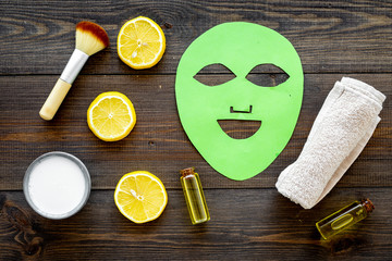 Face spa products. Facial mask, cream, oil, brush near lemon slices on dark wooden background top...
