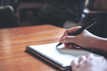 Closeup image of a hand writing down on a white blank notebook on wooden table