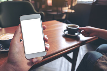 Mockup image of hand holding white mobile phone with blank screen with woman drinking coffee in modern cafe