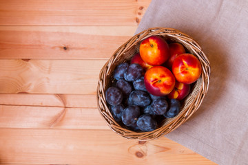 Wicker basket with nectarines and plums on wooden background. Top view.