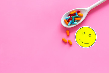 Reception of medicines concept. Recovery. Pills in spoon near smile face emoji on pink background top view copy space