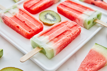 Close-up of a multicolored fruit frozen smoothies with round pieces of kiwi and triangular pieces of watermelon in a white plate on a gray marble background.Dietary summer dessert - Powered by Adobe