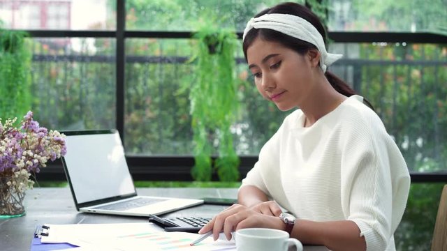 Beautiful young smiling asian woman working on laptop while sitting in living room at home. Asian business woman working document finance and calculator in her home office. Enjoying time at home.