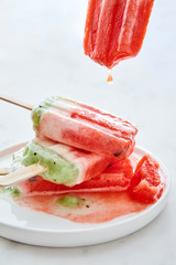 Fruit melting ice cream, drops dripping into a plate with a stack of ice cream around a white marble table with space for text.