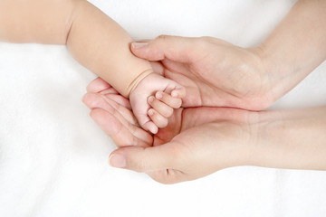 Obraz na płótnie Canvas 赤ちゃんの小さな手を包むお母さんの大きな両手のアップ。成長と健康を喜ぶ母。母性、愛情、幸せ、育児、健康のイメージ