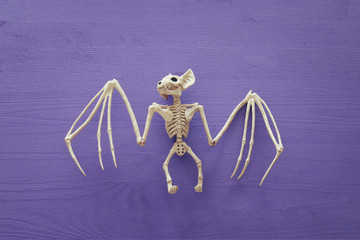 Halloween holiday minimal top view image of bat skeleton over purple wooden background.