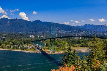 Lions Gate or First Narrows Bridge in Stanley Park Vancouver Canada with North Vancouver and mountains in the background - obrazy, fototapety, plakaty