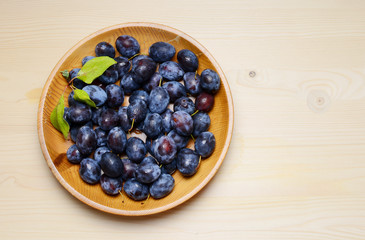 Fresh plums with leaves on a wooden table background. Flat lay composition.