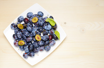 Fresh plums with leaves on a wooden table background. Flat lay composition.