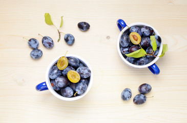 Fresh plums with leaves on a wooden table background. Flat lay composition.
