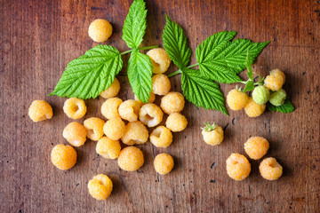 Fototapeta na wymiar Ripe yellow raspberries with leaves on the old wooden background. Top view
