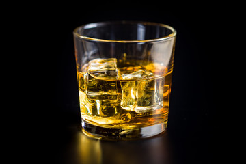 Glass of alcoholic drink with ice cubes on black table.