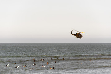 A view of a flying fire helicopter over the Malibu beach and surfers in summer time in California