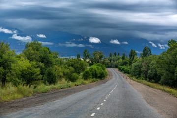 Fototapeta premium Mountain road. Landscape with rocks, sunny sky with clouds and beautiful asphalt road in the evening in summer. Vintage toning. Travel background. Highway in mountains. Transportation