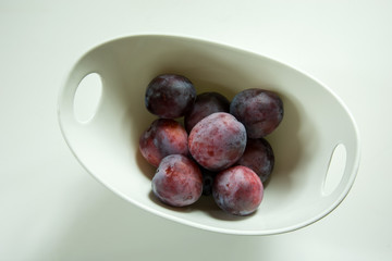 Violet plums in a white bowl on a white background