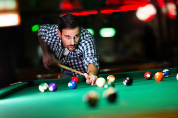 Young attractive man playing pool in bar