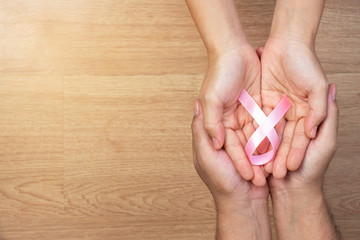 Women's health care concept. Man hands and women hands holding pink bow, pink ribbons, on wooden background, Breast Cancer concept.