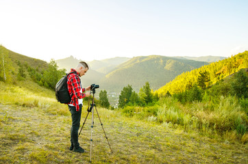 Young guy photographer takes pictures of nature with mountains on a SLR camera.