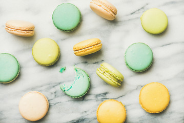 Flat-lay of sweet colorful French macaroon cookies over grey marble background, top view, horizontal composition