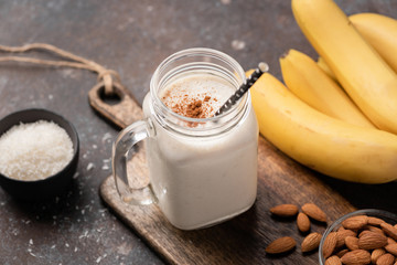 Banana protein smoothie or milkshake with cinnamon and coconut in a drinking jar with staw. Closeup view, selective focus - obrazy, fototapety, plakaty