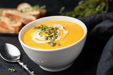 Pumpkin cream soup with pumpkin seeds and cream in white bowl, closeup view. Autumn comfort food