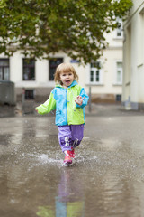 Naklejka premium Kleines Kind läuft in Regen durch Wasser Lacke. Little child girl running happy trough puddle.