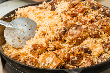 Tasty Uzbek pilaf in a cauldron on fire in the open air at street food festival
