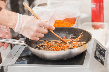 Chef hands in gloves cooking wok noodles in pan