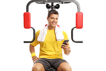 Obraz premium Young man sitting on an exercising machine and holding a mobile phone