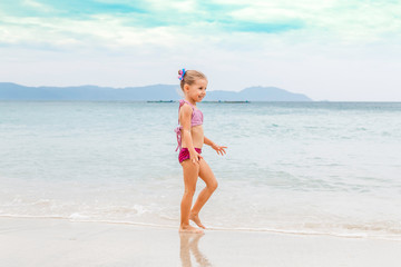 Little beautiful girl dressed in swimsuit stands on the seashore