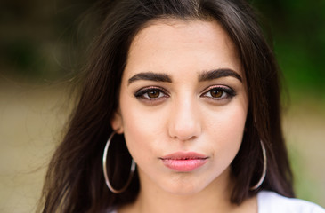 Woman confident face make up looks at camera. Beauty of arabian women. Girl wears big metallic ring earrings. Girl attractive gorgeous brunette middle eastern appearance close up defocused background