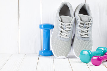 Sport and fitness symbols - sneakers, and colorful dumbbells on wooden wall background