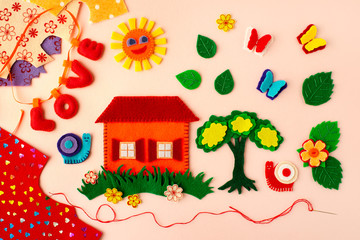 Crafts made of felt on a pink background. House, tree, butterfly, sun, snail are crafts made from colorful felt. Creativity in the form of needlework. View from above.
