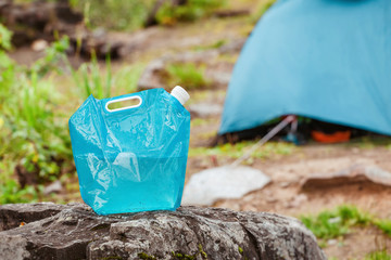 A large bottle or a water tank on a camping background with a tent in the woods