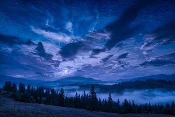 Fototapeta na wymiar Mountain valley with stars in a cloudy night sky