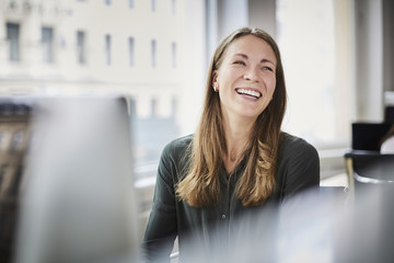 Smiling businesswoman looking away while sitting by window at office