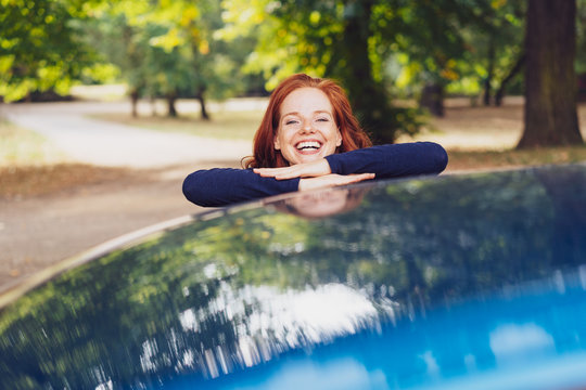Laughing young woman leaning on a blue car
