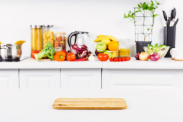 empty cutting board on table with ripe vegetables on background in light kitchen