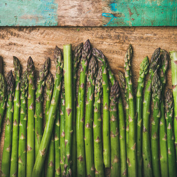 Seasonal harvest produce . Flat-lay of raw uncooked green asparagus in row over rustic wooden background, top view, square crop. Local market food concept
